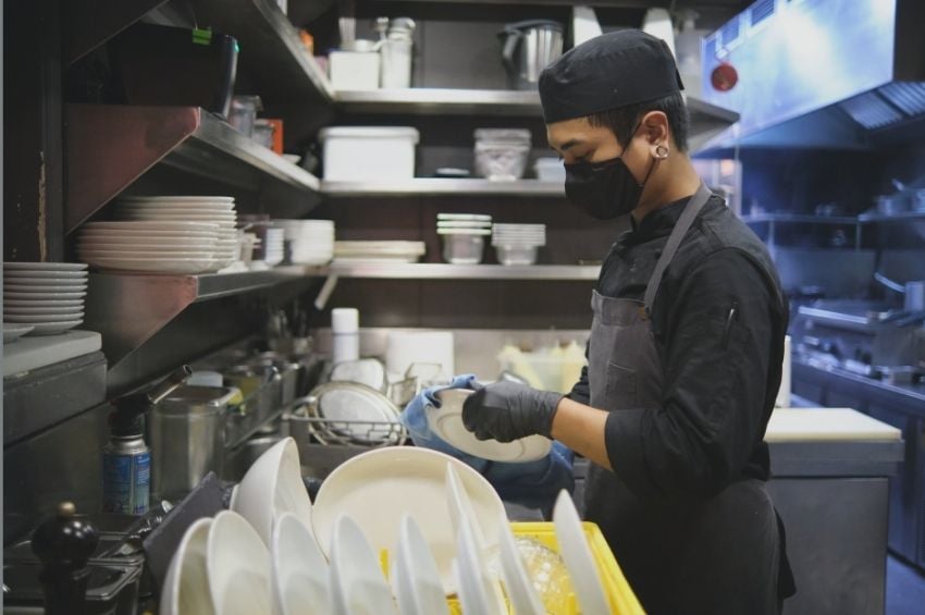 Foodservice worker washing dishes according to cleaning and sanitizing standards