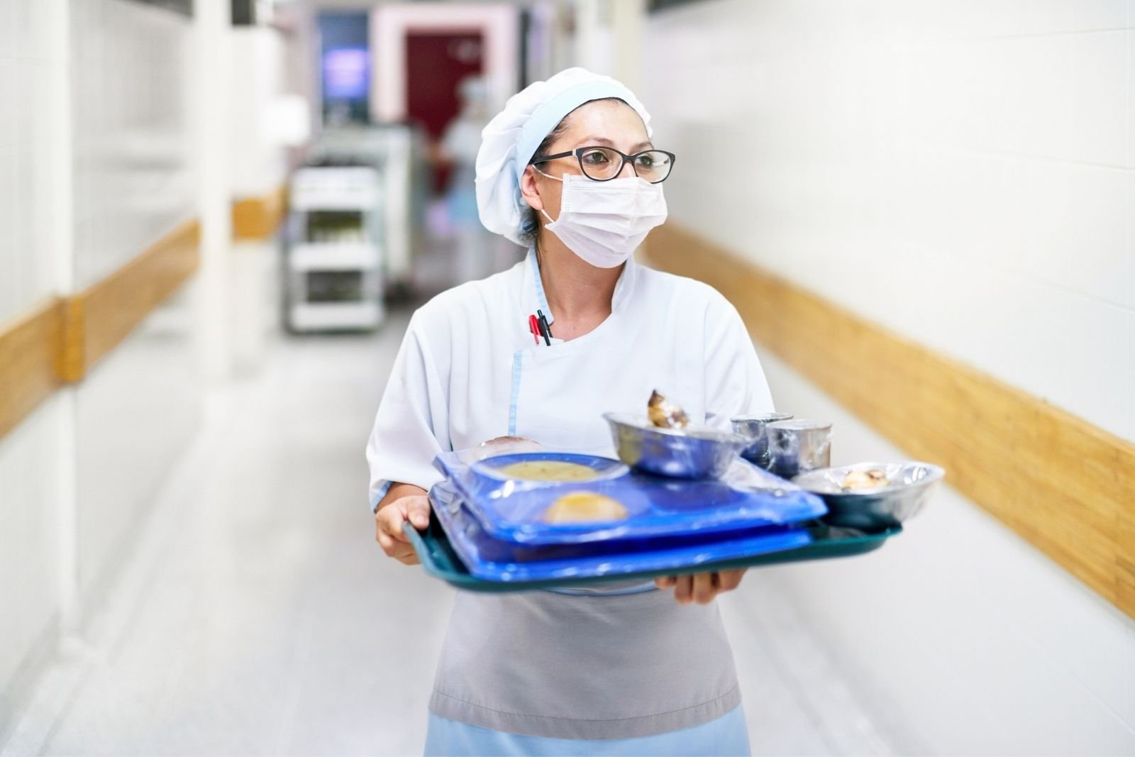Food handler in healthcare carrying a tray of food