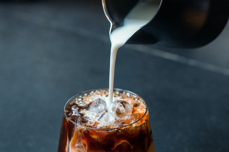 Milk pouring into iced coffee in a clear glass
